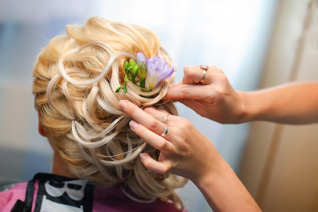 Women's hands make a hairstyle for a blonde bride with flowers