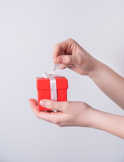 Women's hands open red holiday gift box with white ribbon. Front view