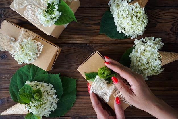 Women's hands pack a gift in a craft box with hydrangea flowers