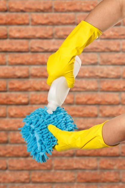 Women's hands in protective gloves with bottle of washing liquid