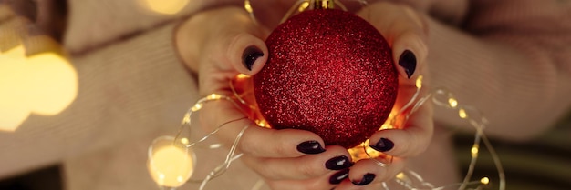 Women's hands in a sweater hold a Christmas ball with garland lights New year and christmas concept Copy space web banner