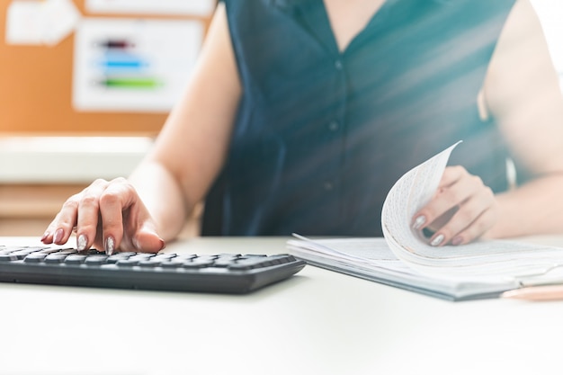 Women's hands typing on the keyboard and leaf through the documents.