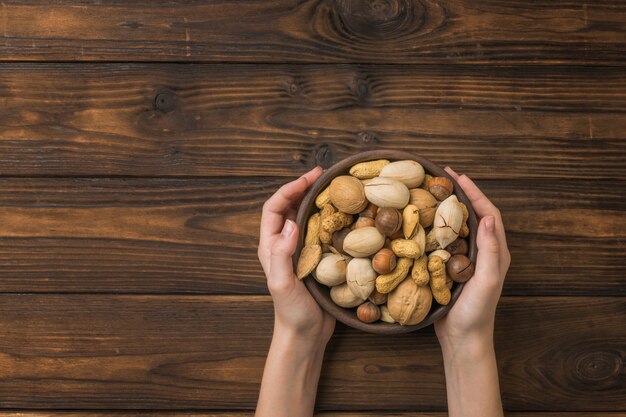 Women's hands with a bowl filled with nut mixture on a wooden rustic table.