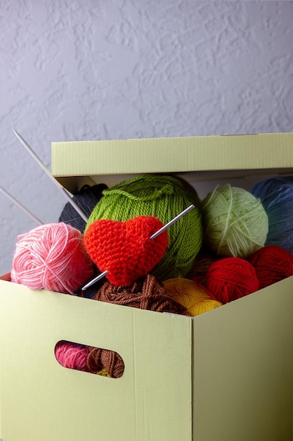 Women's hobby knitting. Yarn of bright colors, a knitted heart lies in a needlework box on a gray background.