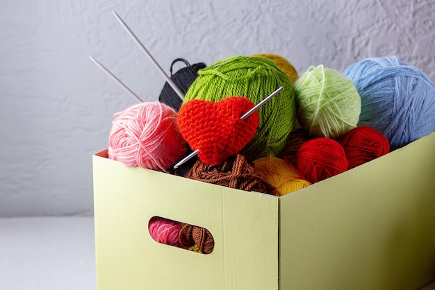 Women's hobby knitting. Yarn of bright colors, a knitted heart lies in a needlework box on a gray background.