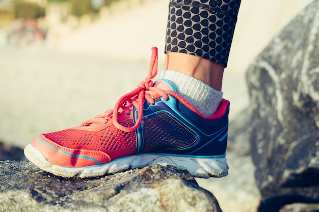 Women's leg in red and blue sneaker standing on a rock in the morning sun