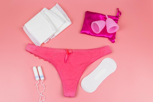 Women's panties with menstrual cups sanitary pads and tampons on pastel pink background Top view Concept of critical days menstruation feminine hygiene