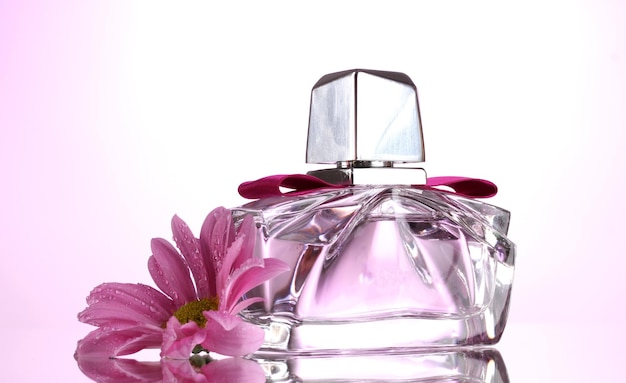 Women's perfume in beautiful bottle and flower on pink background