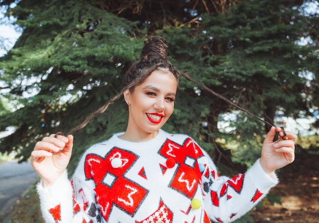 Women's style A beautiful woman with red lips makeup on her face and hairstyle in a winter New Year sweater on the background of a Christmas tree high quality