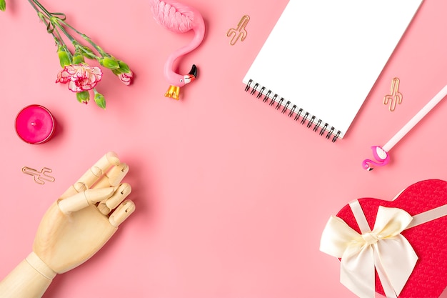 Women's things - notebook, flamingo, pen, carnation flowers, wooden hand, candle, paper clips cactus, gift box heart on pink background