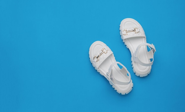 Women's white leather sandals on a blue background Minimal concept of summer women's shoes