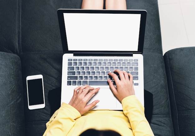 Women sit on a black sofa and using a blank screen laptop and smartphone.