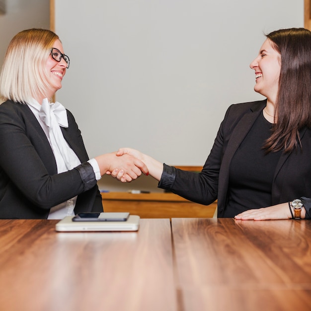 Women sitting at table shaking hands smiling