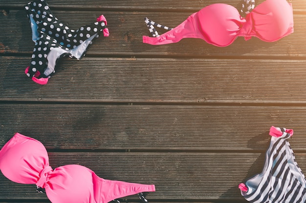 Women swimsuit lying on wooden background. Top and bottom part of swimwear. Colorful. Pink and black with white stripes