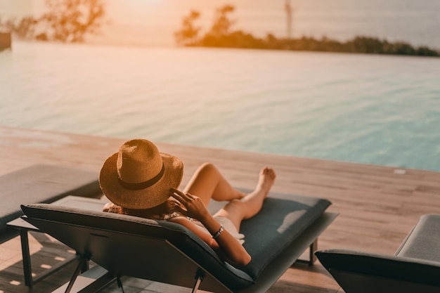 Women tourists are lying on the bed by the pool watching the sunset.