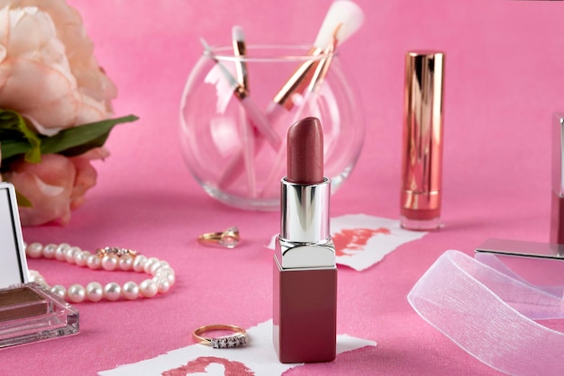 Womens cosmetics makeup brushes lipstick and gold jewelry lying on a pink background