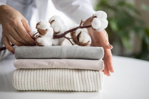 Photo womens hands hold a stack of neat clean cotton clothes in neutral shades branch with cotton