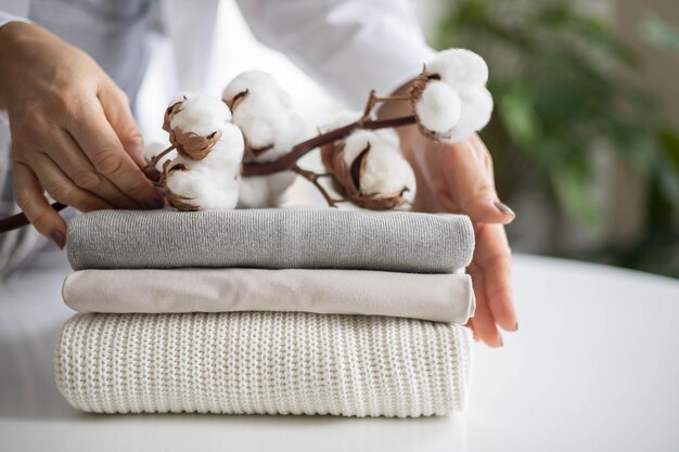 Photo womens hands hold a stack of neat clean cotton clothes in neutral shades branch with cotton