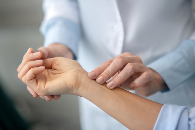 Womens neat experienced doctor hands gently palpating patients forearm, finding the painful area