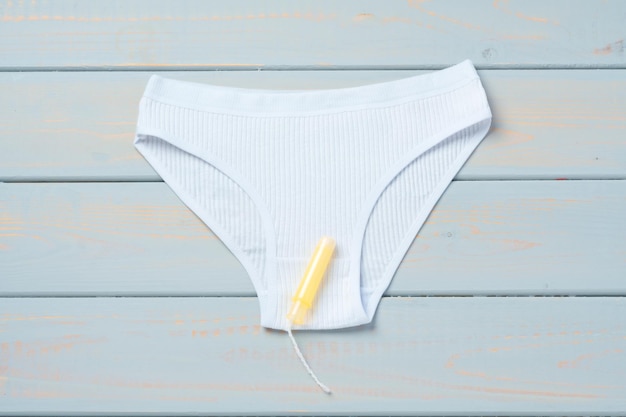 Womens panties with sanitary tampon on color background