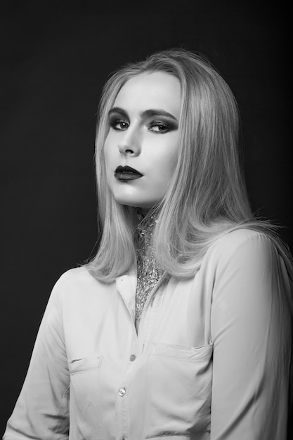 Photo wonderful blond model posing at studio with bright makeup and foil on her neck. monochrome shot