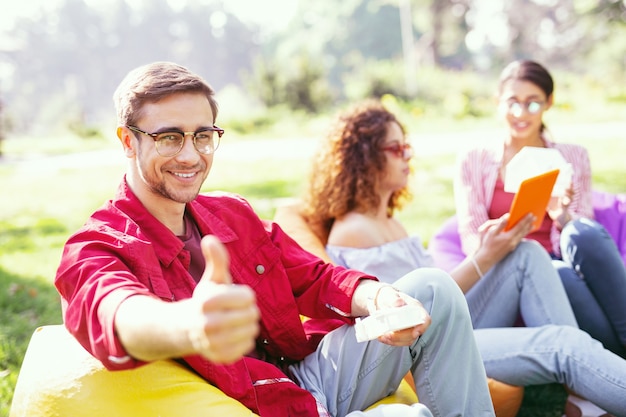 Wonderful day. Handsome cheerful man smiling and working with his colleagues in the open air