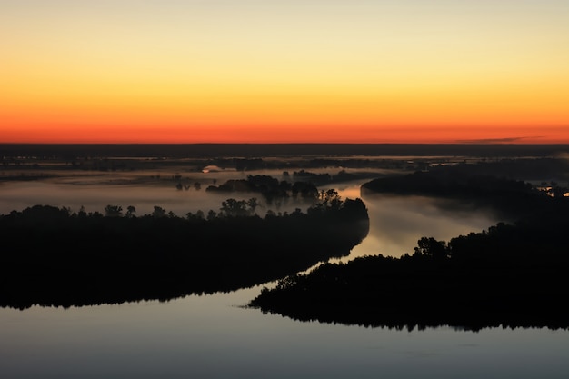 Wonderful ghostly foggy dawn above silhouette of island and misty river.