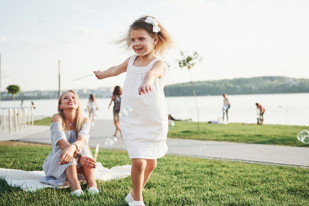 A wonderful girl child makes bubbles with her mom in the park.