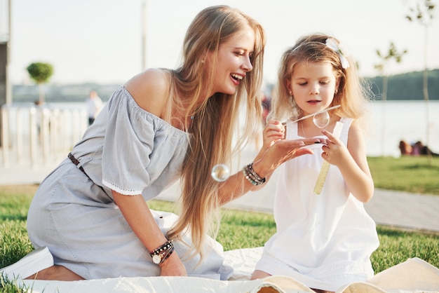 A wonderful girl child makes bubbles with her mom in the park.