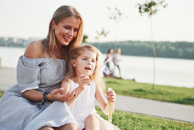 A wonderful girl child makes bubbles with her mom in the park.