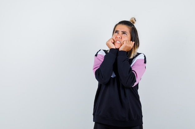 Wonderful lady keeping fists on cheeks in sweatshirt and looking enraged