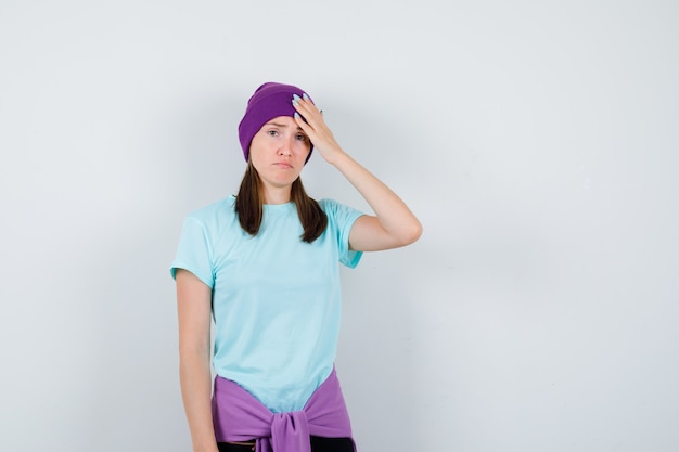 Wonderful lady keeping hand on head in blouse, beanie and looking upset , front view.