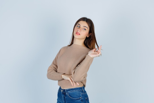 Wonderful lady in sweater, jeans playing with her hair and looking charming , front view.