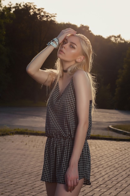 Wonderful tanned blonde woman with long hair wearing black romper, posing in sun glare