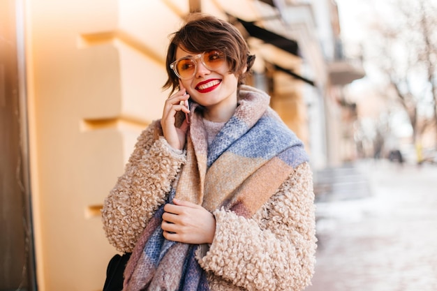 Wonderful young woman talking on phone on street Outdoor shot of trendy girl in coat and scarf