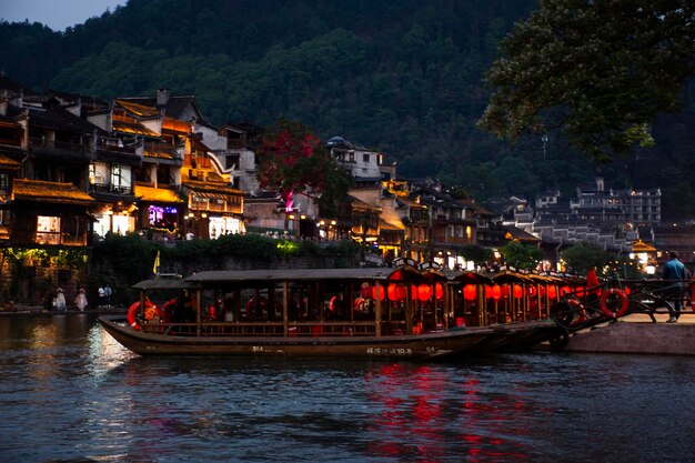 Photo wood boat in toujiang river for service tour trip chinese visit historical buildings heritage architecture of xiangxi phoenix ancient city or antique old town feng huang on may 9 2024 in hunan china