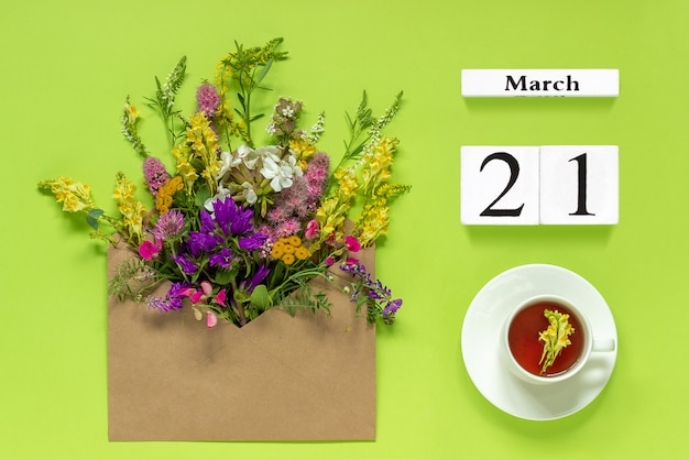 Wood calendar March 21. Cup tea, kraft envelope with colored flowers on green 