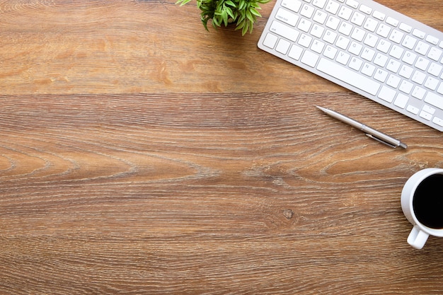 Wood office desk table with computer keyboard, cup of coffee and pen.