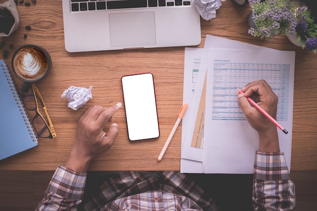 wood office table with businessman checking report paper, blank screen on mobile