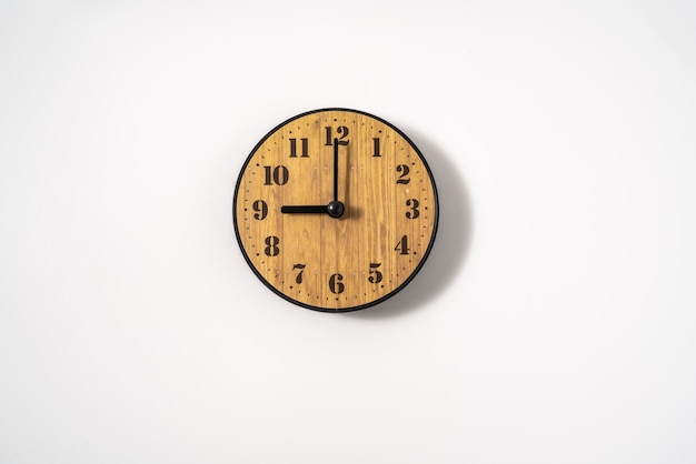 Wood office wall clock with white dial on white wall. wall clock on white background, top view.