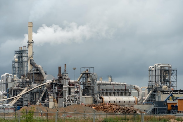 Wood processing plant against the background of gray clouds White toxic smoke comes out of factory chimneys Utopian landscape Environmental pollution An environmental disaster