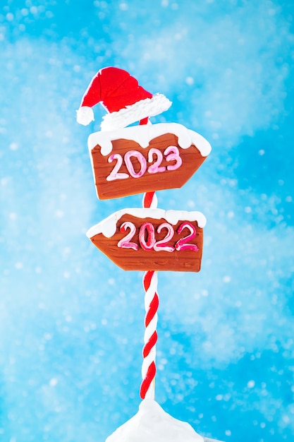 Wooden 2023 and 2022 direction signs and santa hat on blue background