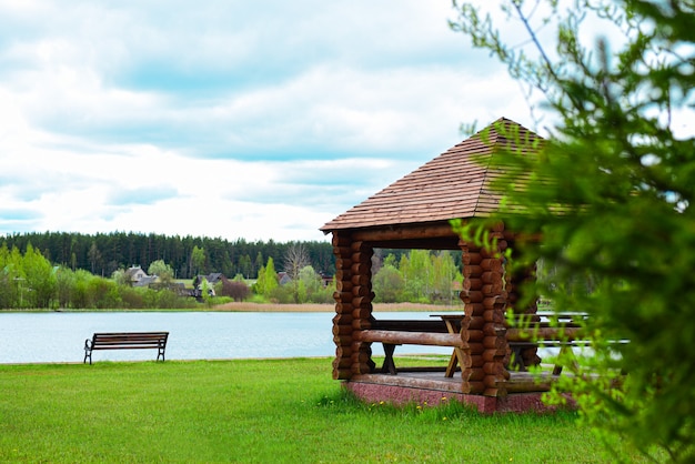 Wooden arbor with a bench on the shore of a forest lake