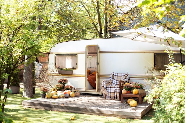 Wooden armchair and flowers in pots near caravan trailer in garden RV house with garden furniture