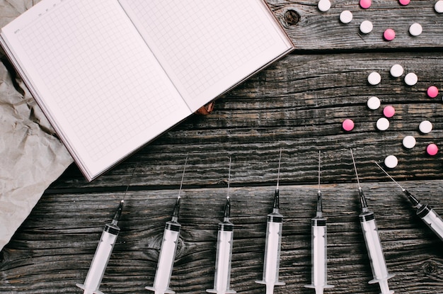 On a wooden background are syringes tablets and a notebook space for writing