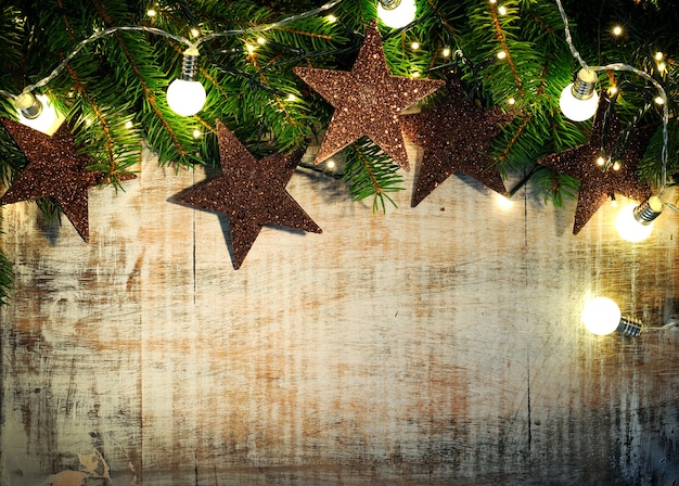 Wooden background with fir twigs, stars and christmas lights