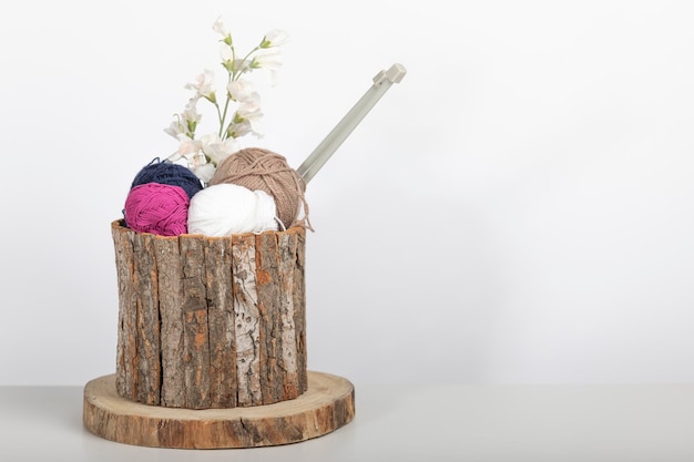 Wooden basket with balls of wool and knitting needles together with a decorative flower on a white background