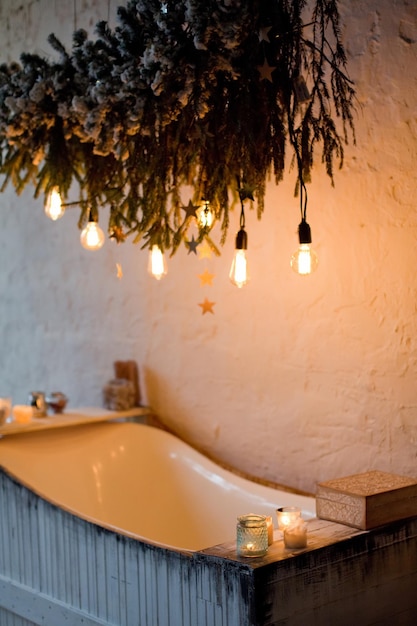 Wooden bathtub with Christmas tree branches and light bulbs decoration Cozy winter batroom