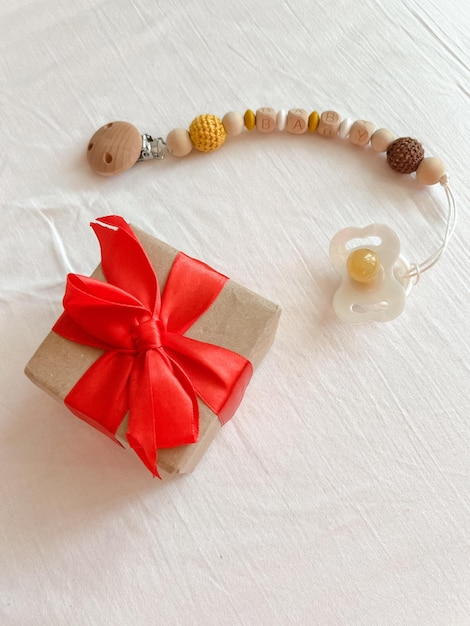 Wooden beadsholders with a pacifier and a gift with a red ribbon are on a white smooth textile surface Christmas gift for a newborn