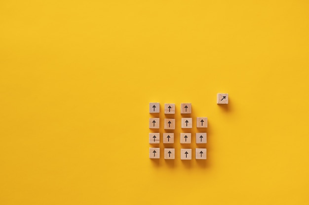 Wooden block with arrow on it separating from a group of other blocks in a conceptual image of vision and determination.